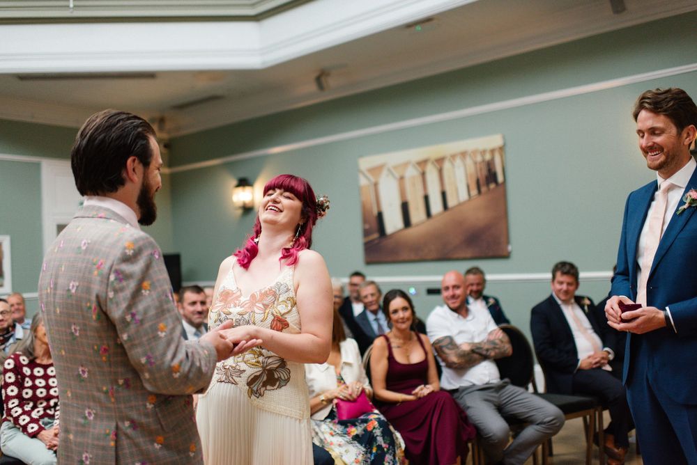 Bride and groom laughing joyfully during wedding ceremony with guests seated behind.
