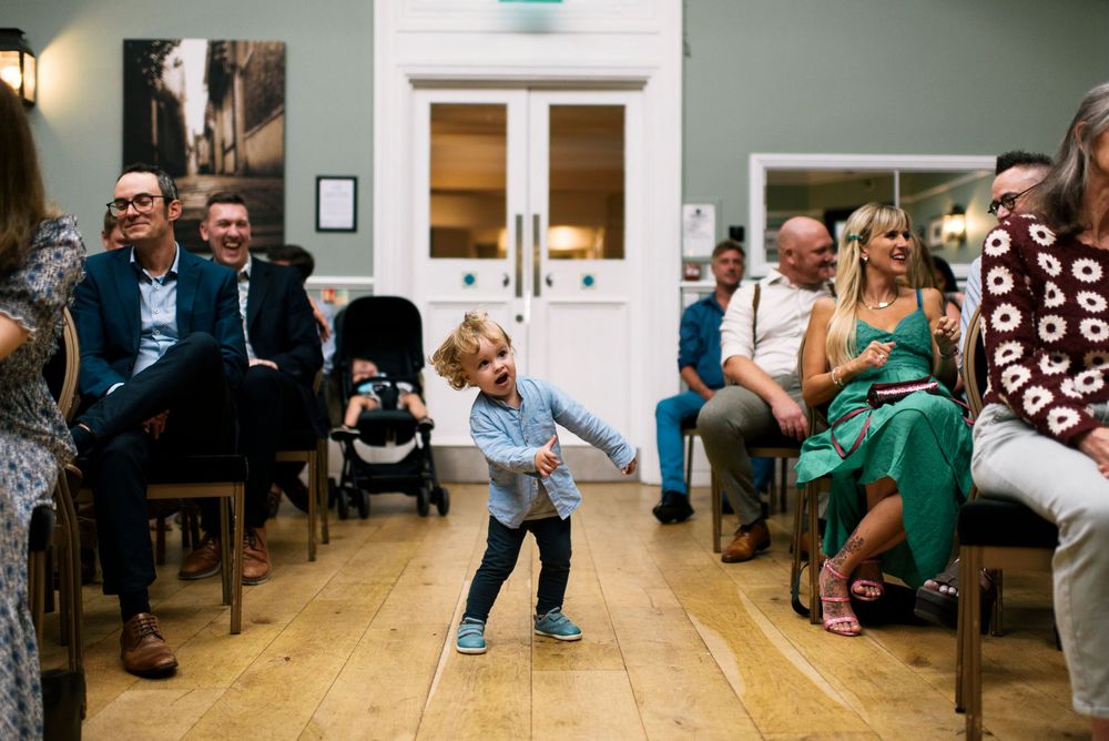 Young child dancing in aisle during wedding ceremony as guests laugh and watch.