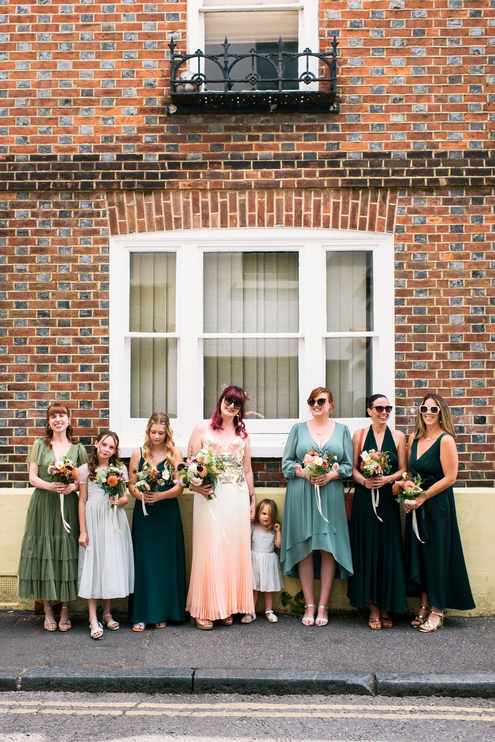 Bride with bridesmaids in mismatched green dresses holding bouquets outside the Hotel Du Vin Brighton.