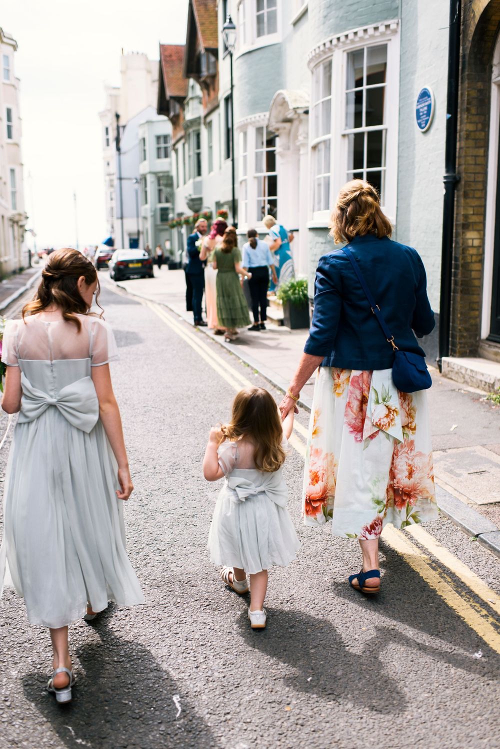 Women and children in wedding attire walking down a charming street in Brighton.