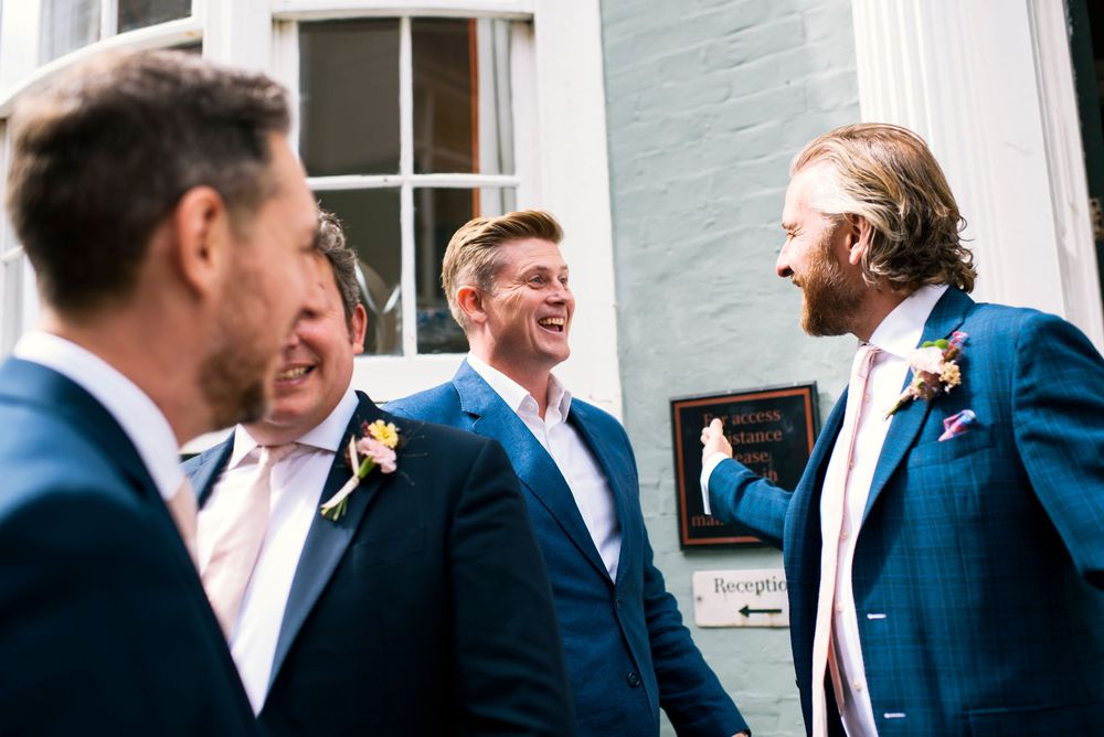Four groomsmen in navy blue suits with floral boutonnieres laughing together outside Hotel Du Vin Brighton.