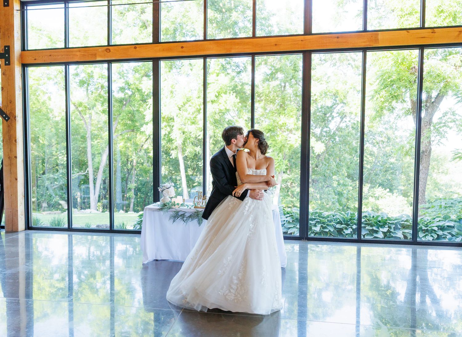 Elegant couple in a bright, modern glass-walled venue share a romantic dance in their wedding attire at Graystone Valley in Branson, MO.