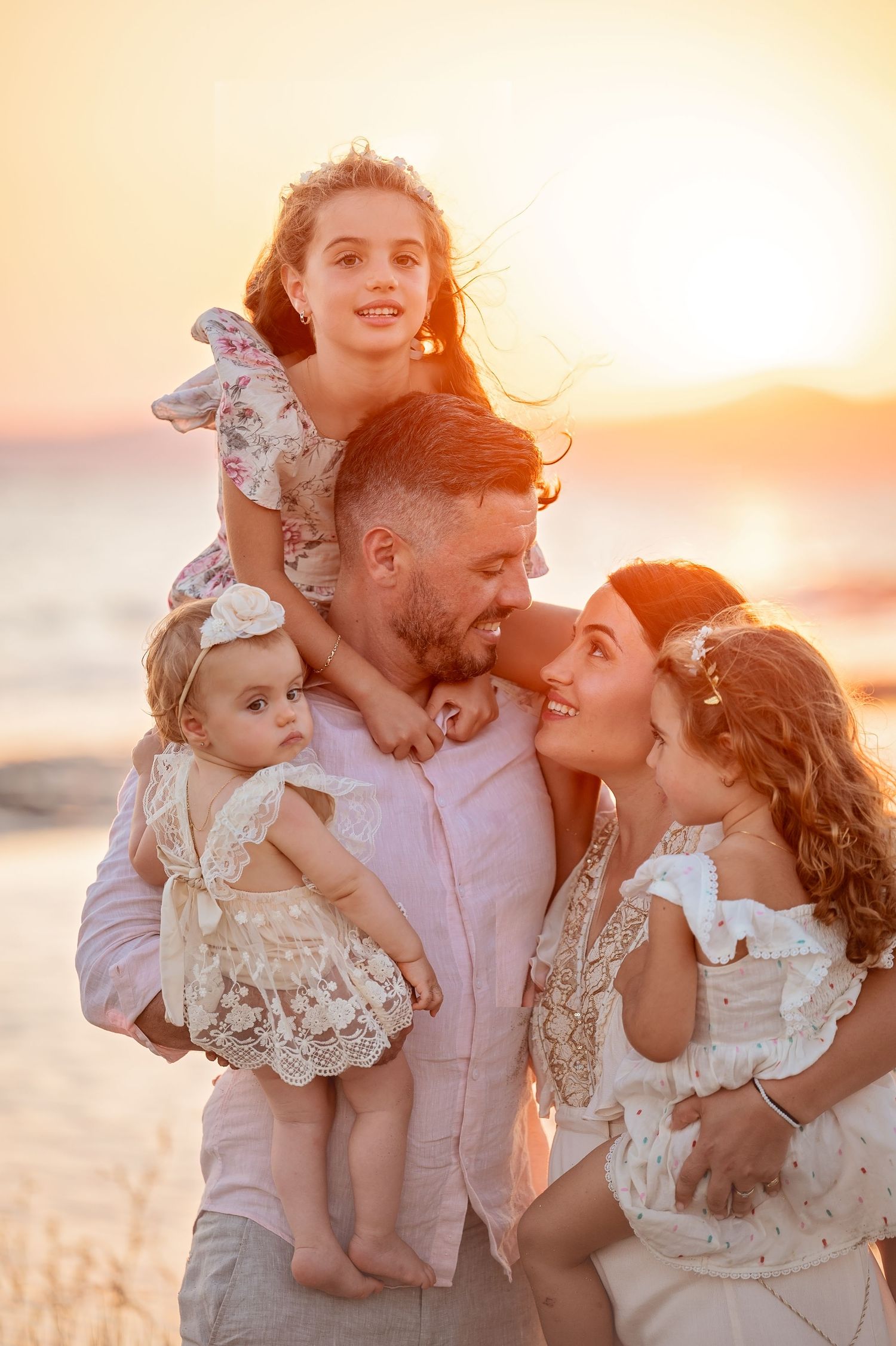 A family wearing light colored clothing embraces during a beautiful beach sunset photoshoot.