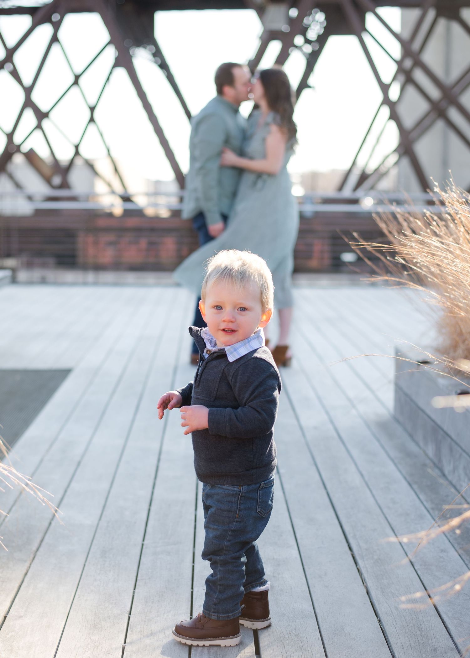 A child wearing a navy puffer vest jumps and plays on a wooden deck during outdoor playtime.