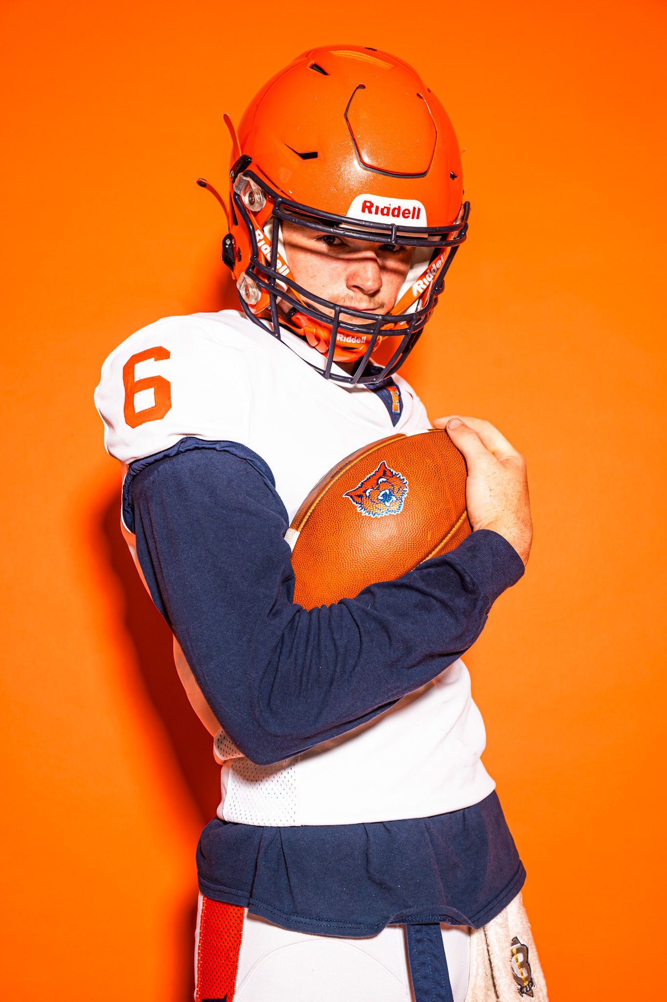 Two people wearing navy and white sports uniforms share an emotional embrace against a bright orange background.