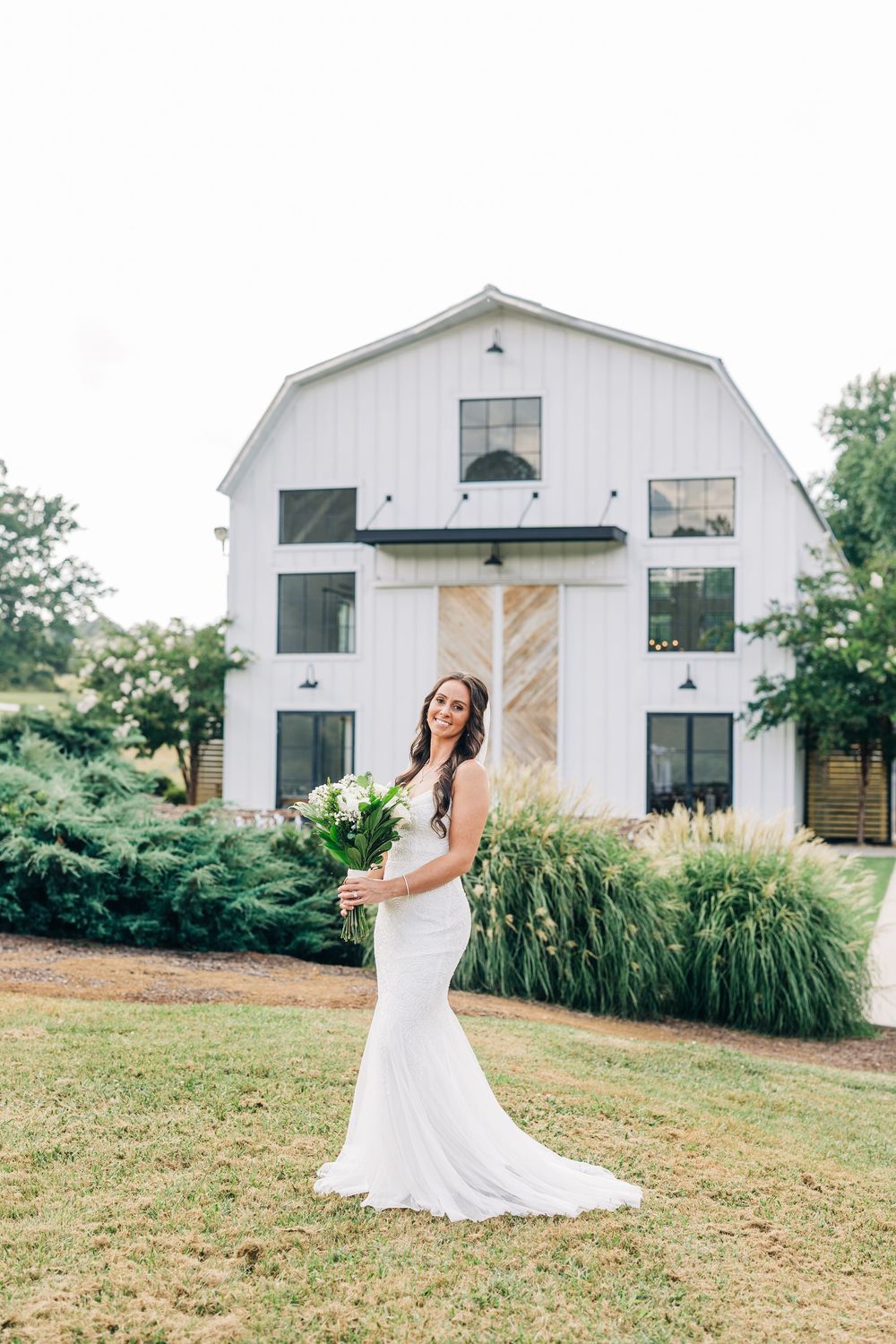 White barn backdrop with rustic charm and green grass fields creates an elegant countryside setting for Bridal Portrait at Barn South