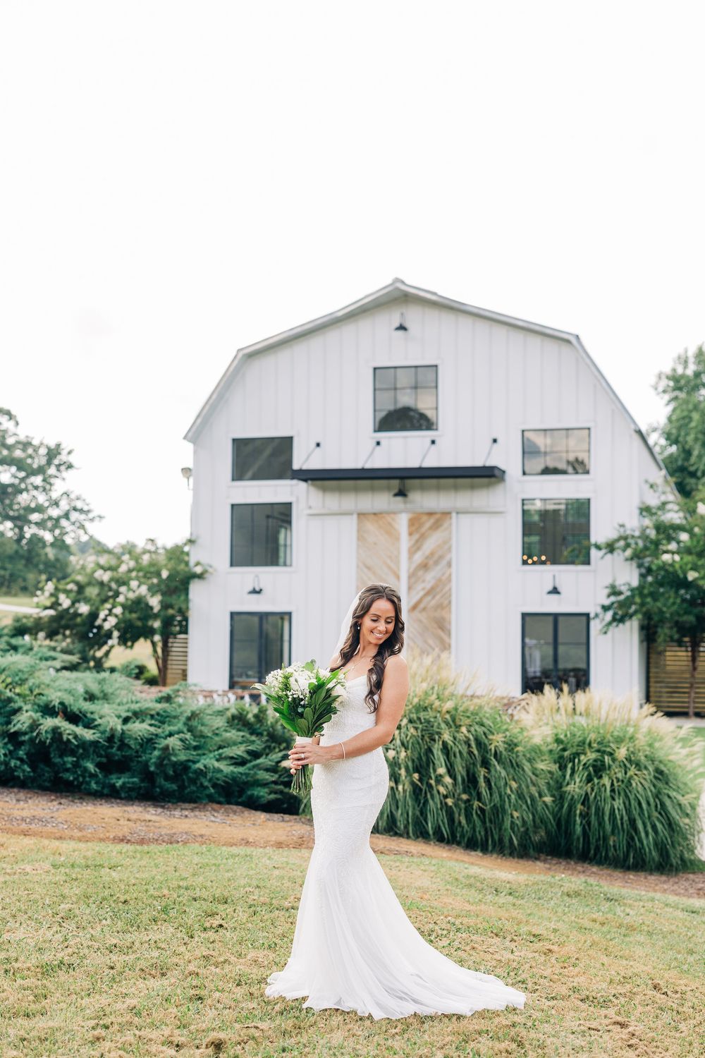 A rustic wedding venue features a white barn and lush greenery in a serene country setting.