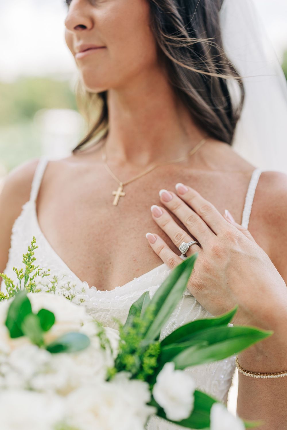 Close-up details of a bride's neckline with delicate jewelry and white floral bouquet.