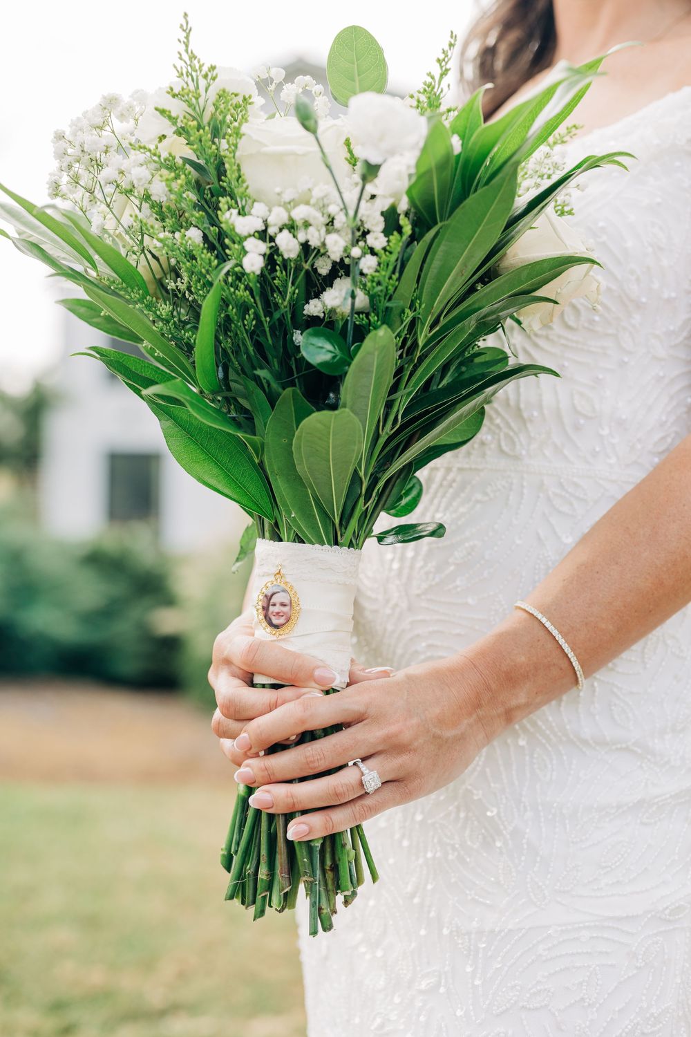 Close-up view of a classic white bridal bouquet with lilies and greenery held against a white lace dress.
