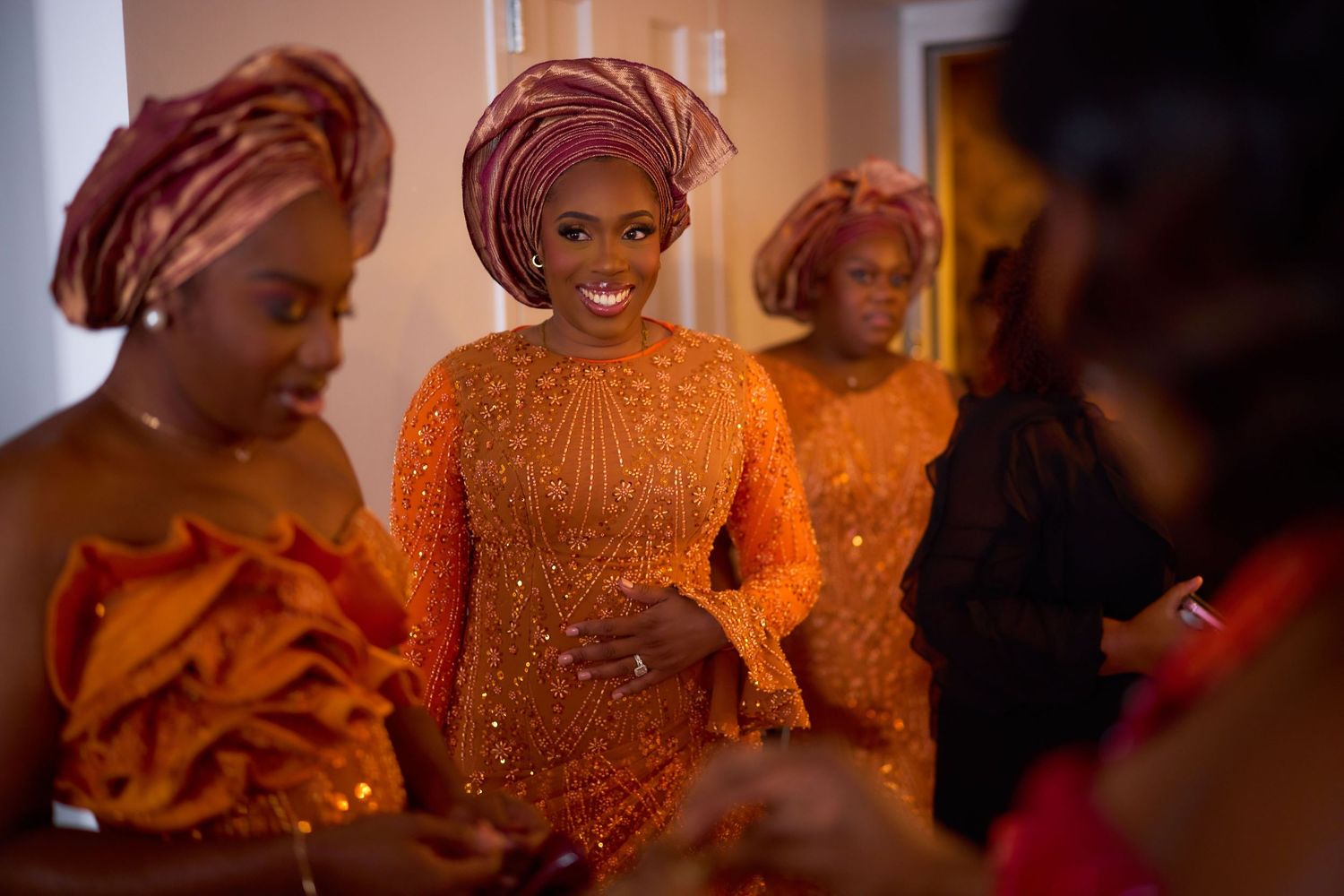 Wedding attendees wearing vibrant orange and gold traditional African attire gather at a celebration event.