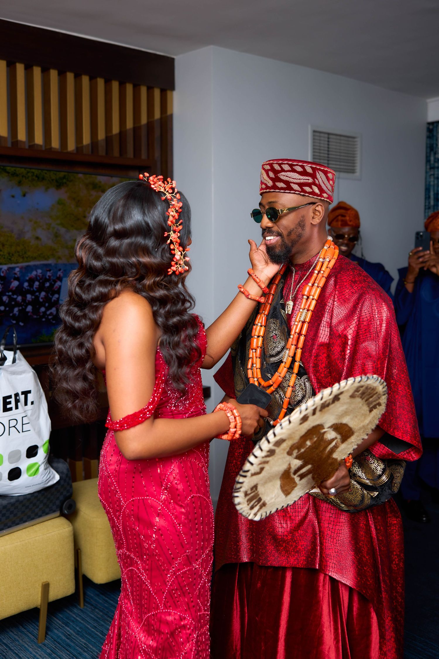 African couple in elegant red attire pose for wedding photos in an indoor setting.
