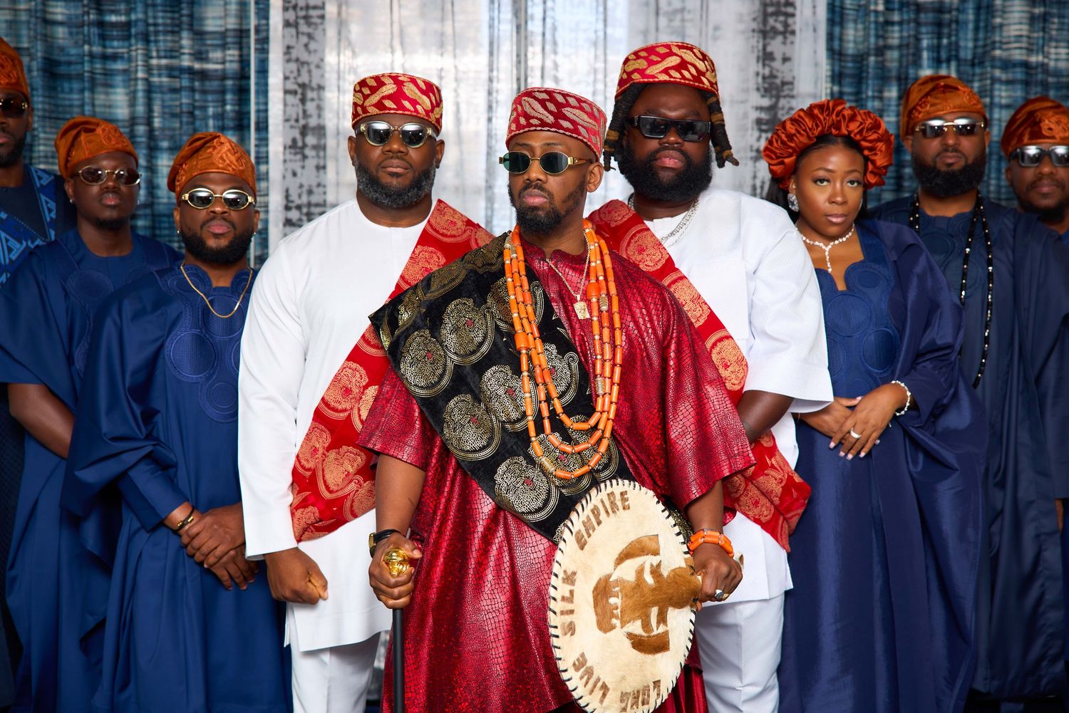 Traditional Nigerian wedding party wearing blue and red attire poses together for formal group photo.