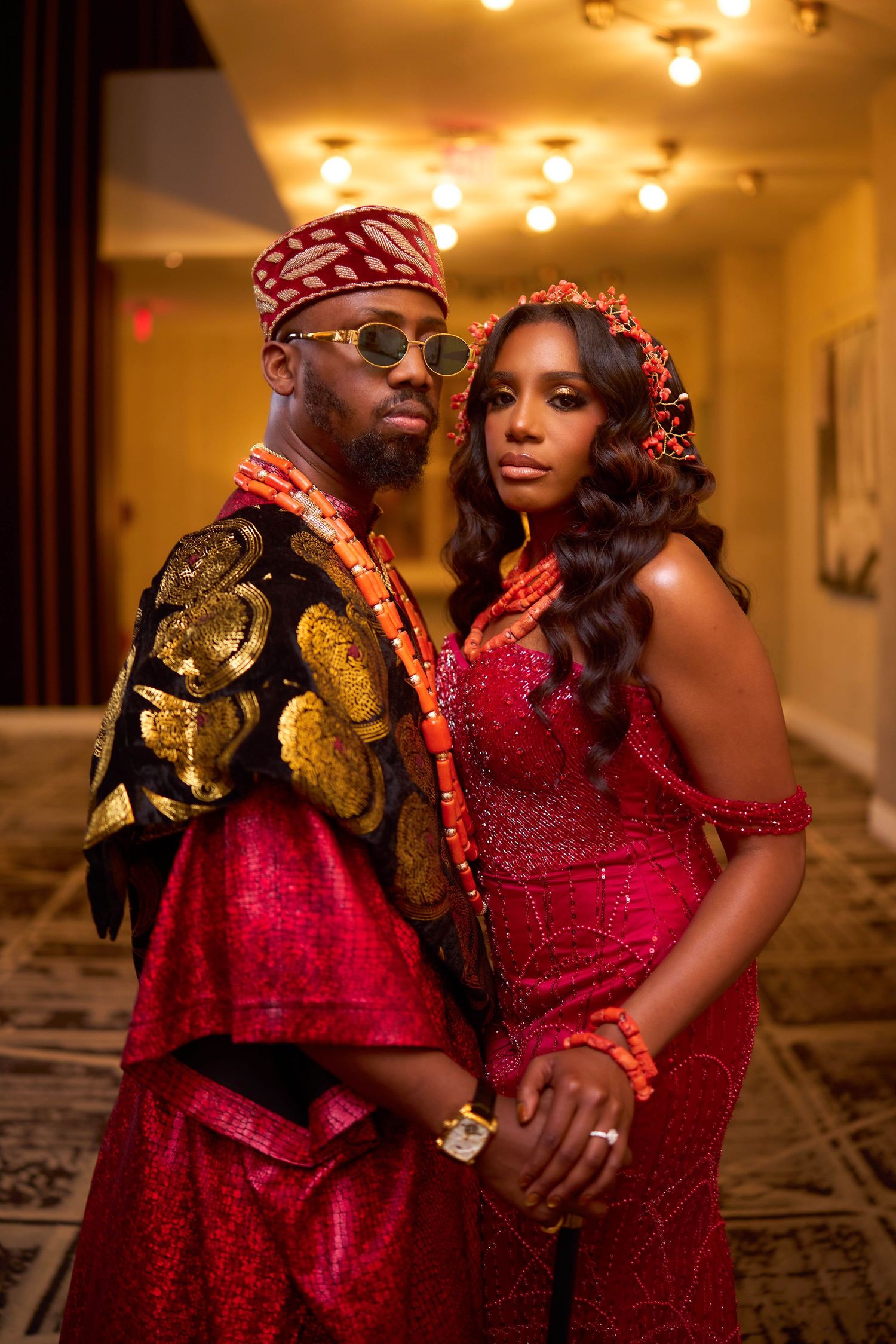 Wedding couple in burgundy sequin dress and printed suit embrace in warmly lit room.