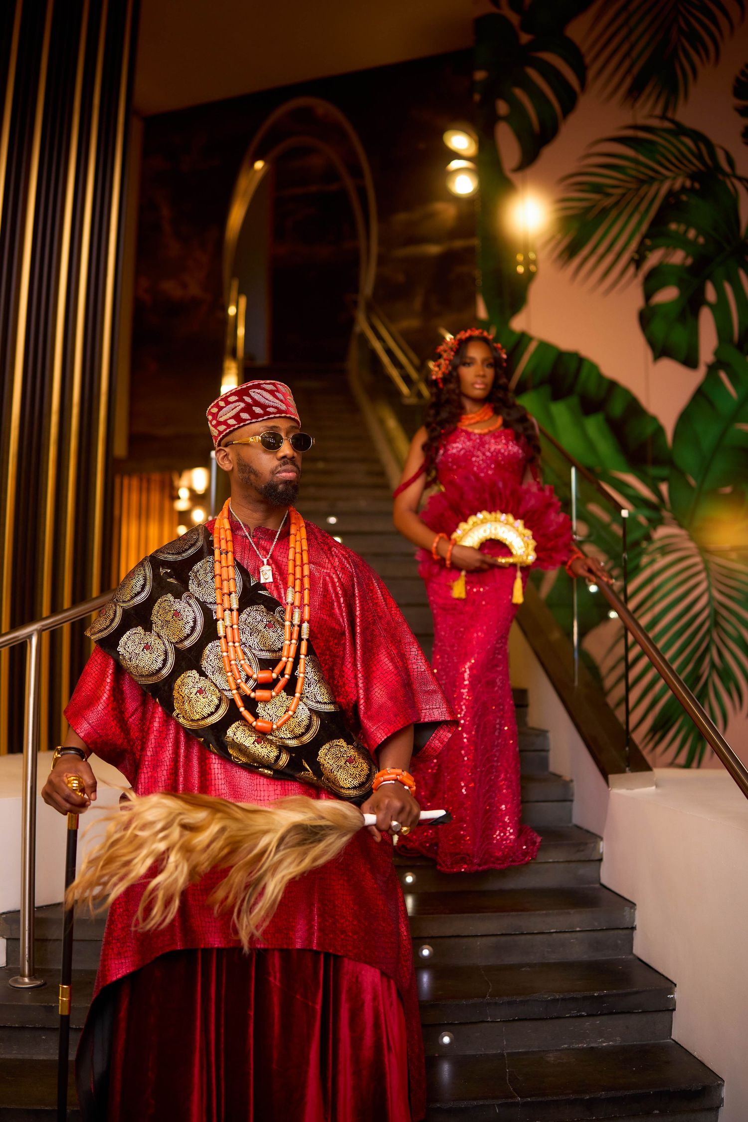 Traditional African attire displayed in rich red garments adorned with ornate gold necklaces and accessories in evening ambiance.