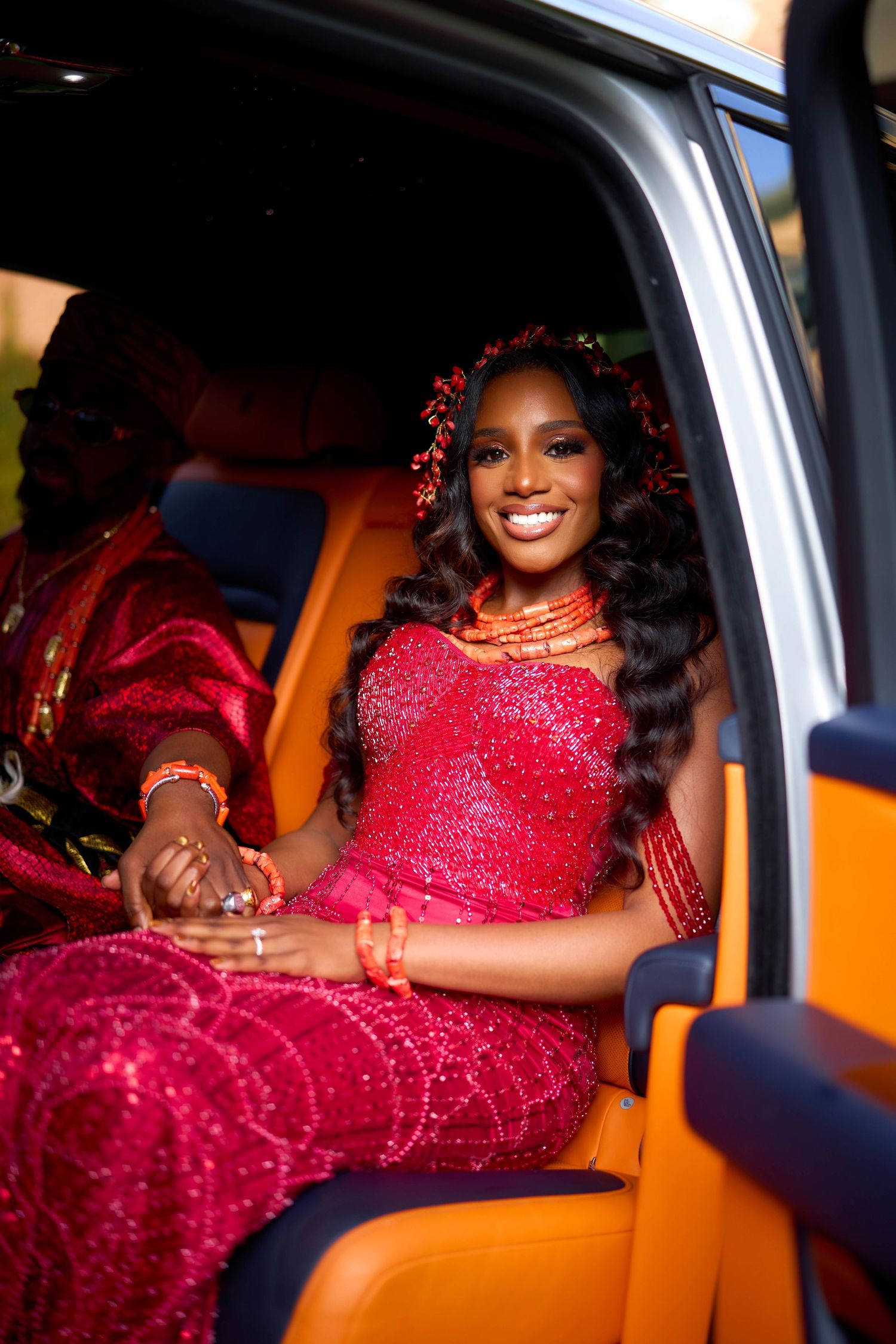 Happy person in a sparkling red gown poses from inside a vehicle at night.