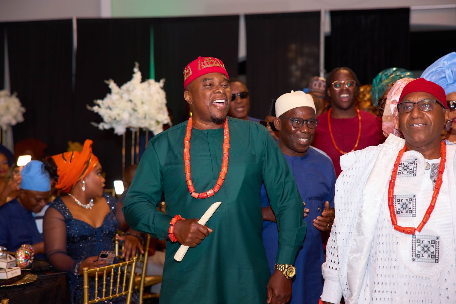 A group of formal event attendees interact and smile while sitting at decorated dining tables.