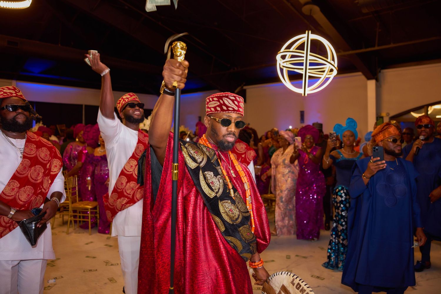 Traditional Nigerian wedding celebration with people in colorful attire dancing and celebrating in an indoor venue.