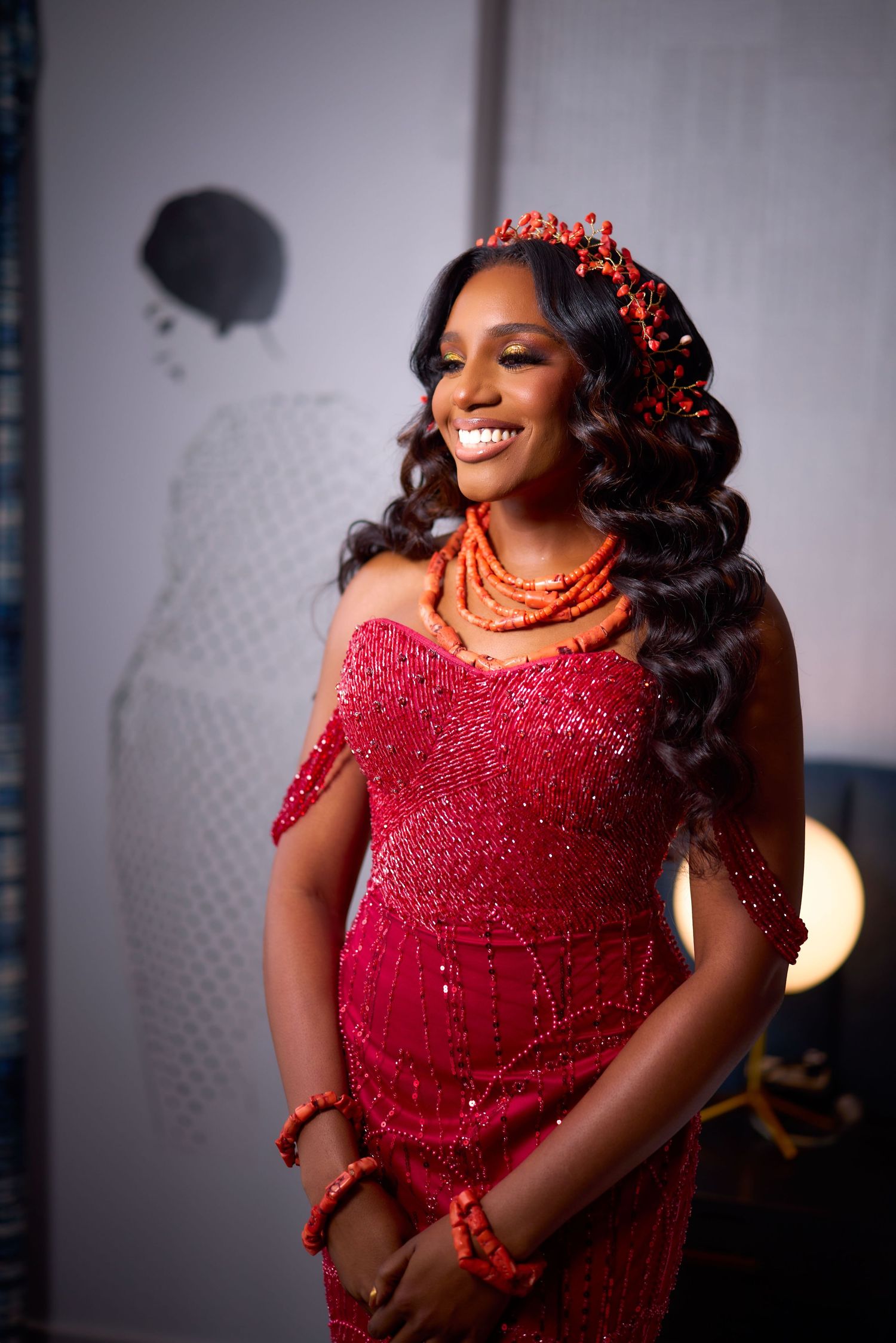 Traditional elegant Nigerian wedding attire featuring a sparkling red dress, coral beaded necklace, and floral headpiece.
