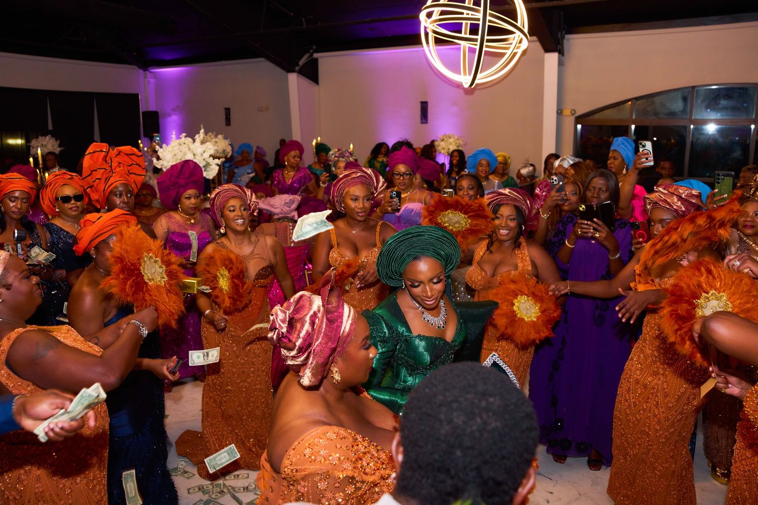 A lively Nigerian wedding reception celebration with guests dancing in traditional attire and colorful headwear.