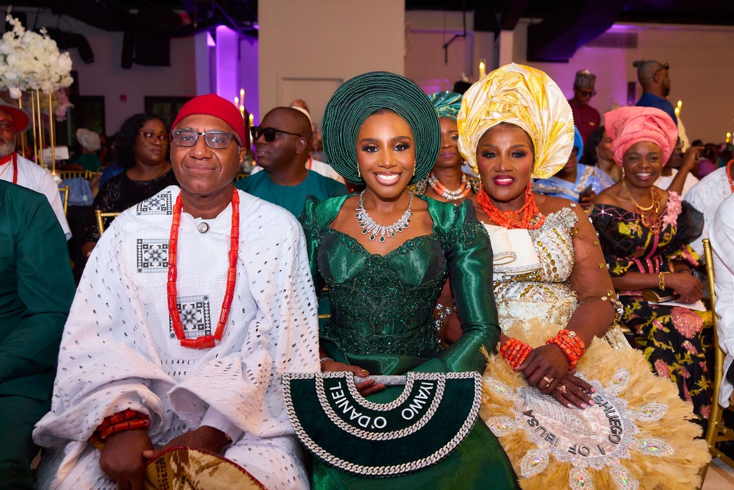 Colorful celebration scene at a Nigerian wedding party with guests wearing traditional attire and vibrant headwraps.
