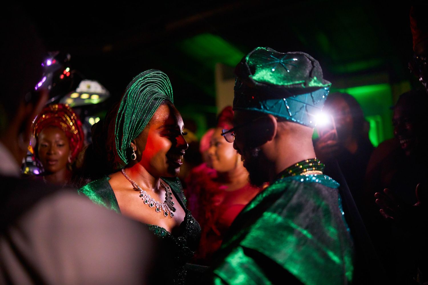 Dimly lit dance floor with green lighting highlighting performers in sparkling emerald costumes.