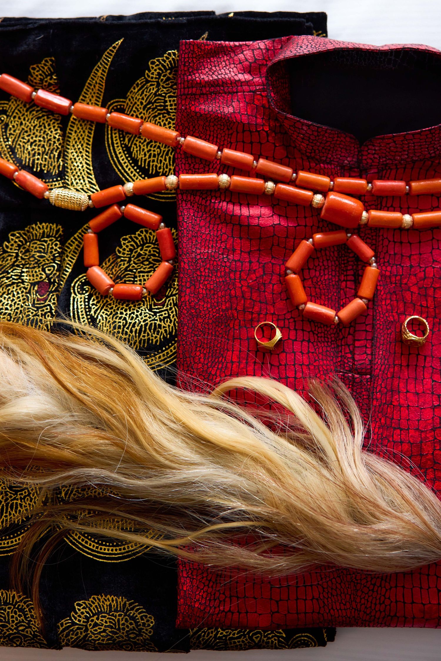 Close-up details of red beaded jewelry and blonde hair against a dark patterned background.