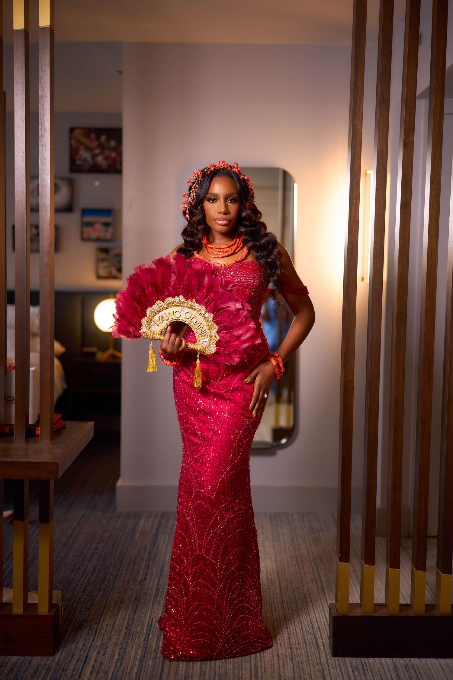 A person wearing a vibrant red sequined dress poses elegantly in a hallway with wooden pillars and ambient lighting.