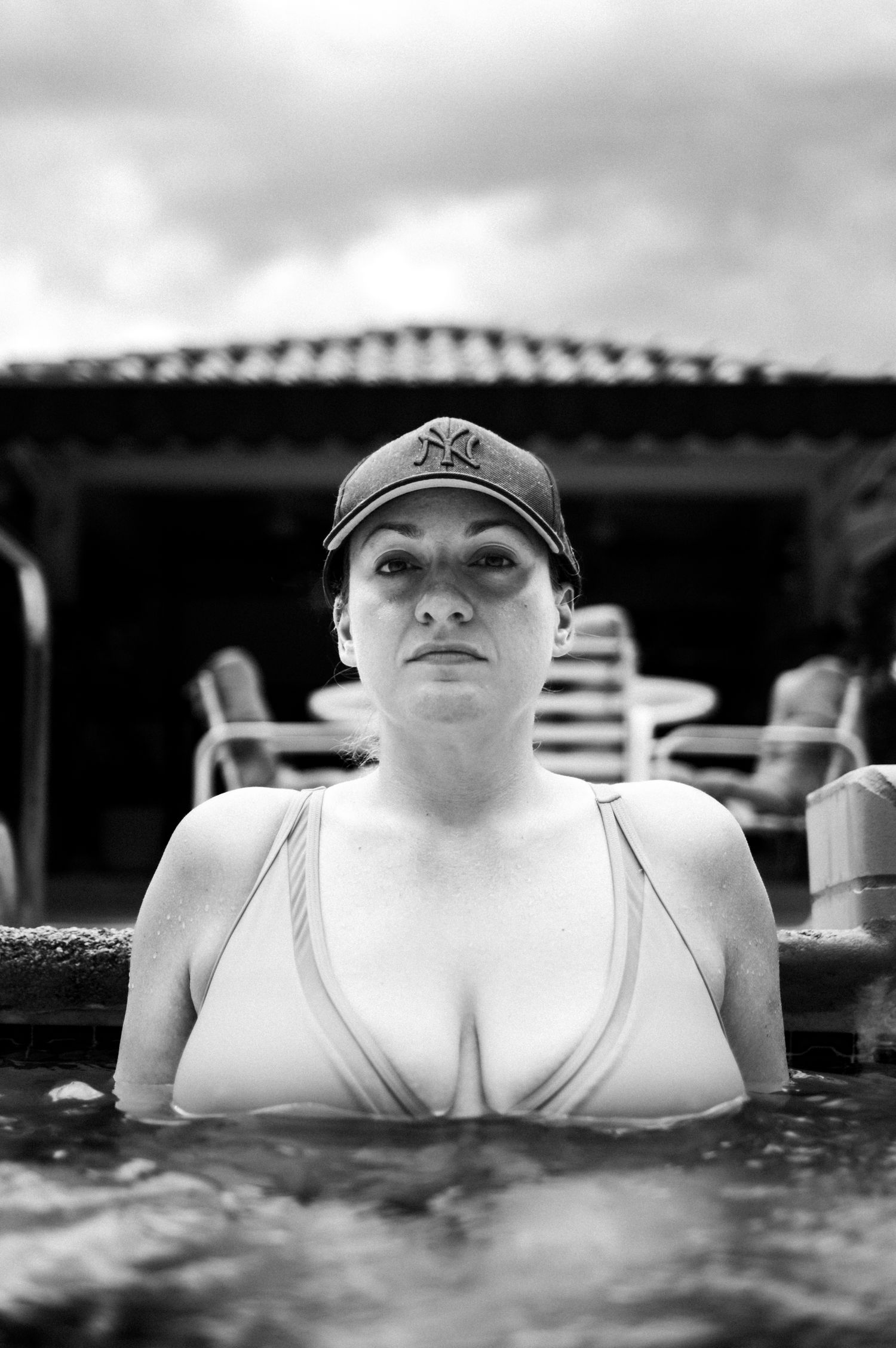A black and white panoramic shot shows someone floating in dark rippling water while wearing a baseball cap.