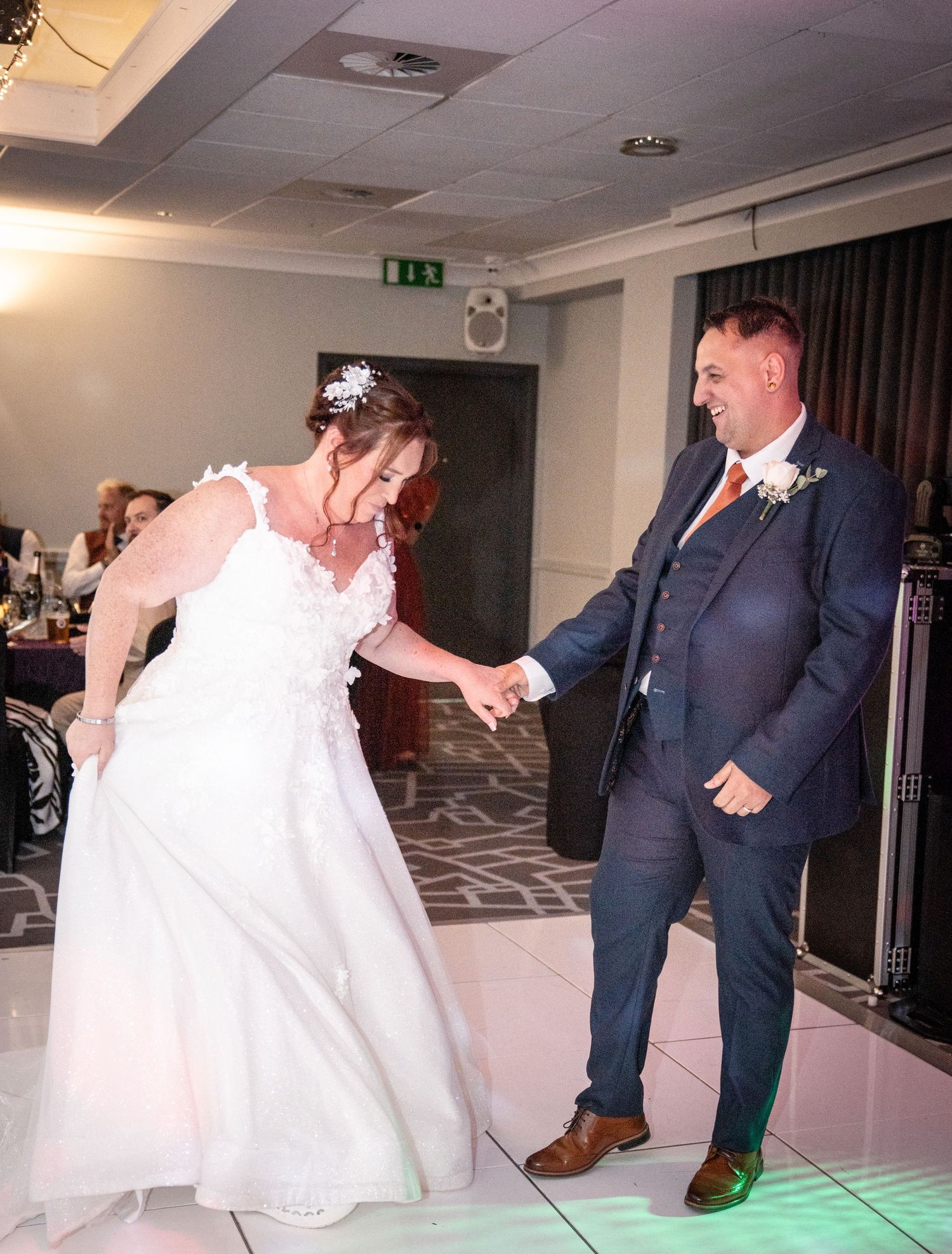 Couple dancing energetically on a white illuminated dance floor at their wedding reception.