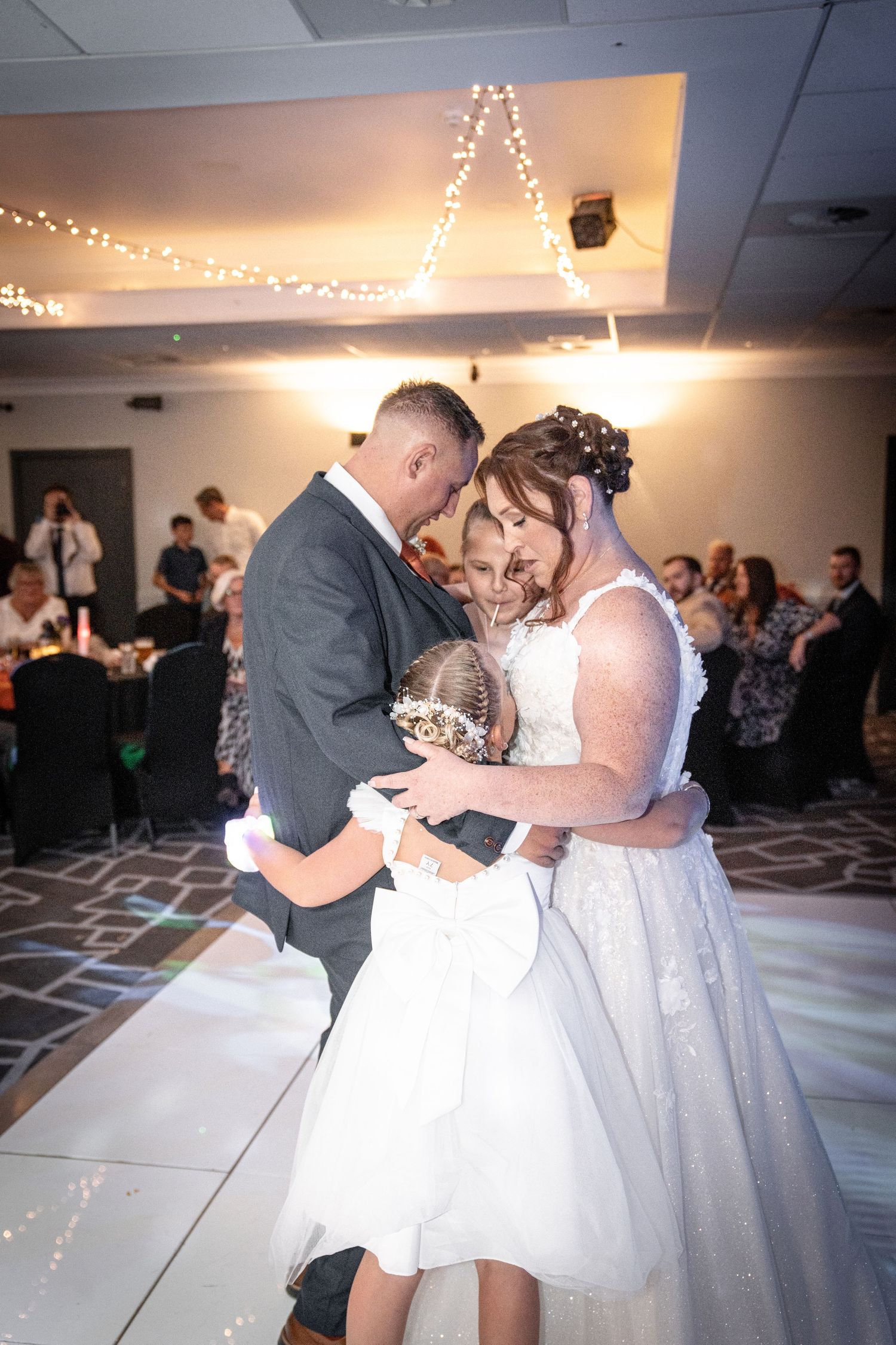 Couples dancing at a wedding reception under string lights in a banquet hall.