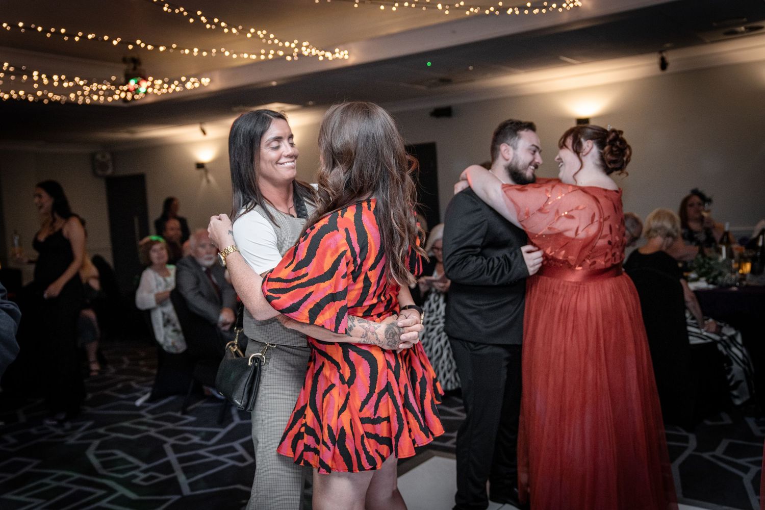 Guests dancing at a dimly lit wedding reception with string lights decorating the ceiling and walls.