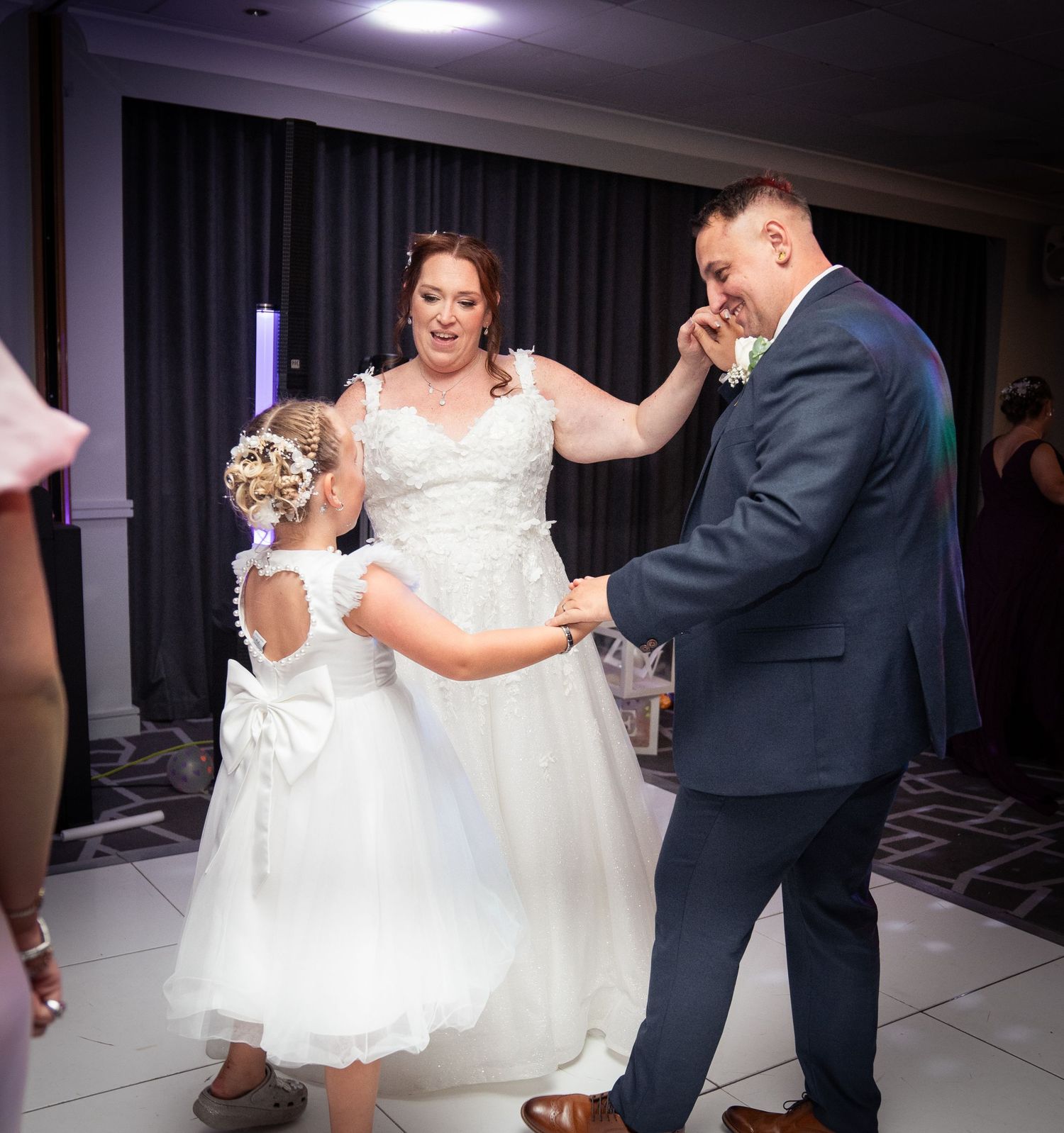 A tender dance moment captured at a wedding reception with a white dress and dark suit on a tiled floor.