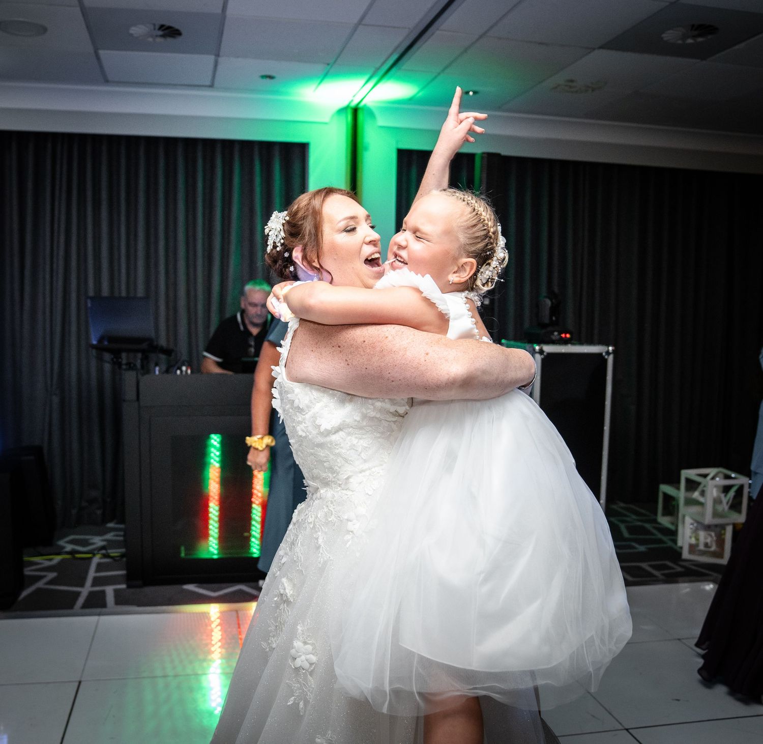 A bride in a white dress dances exuberantly on a dark dance floor lit by green spotlights.
