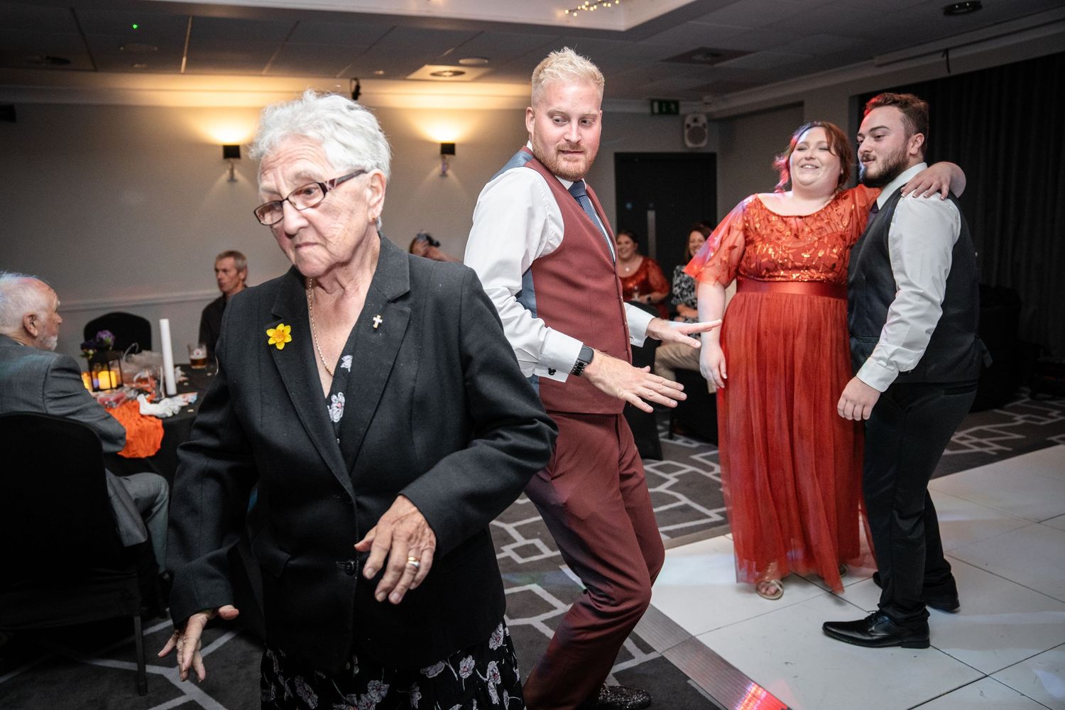 Wedding guests dancing and socializing at an evening reception with ambient lighting.