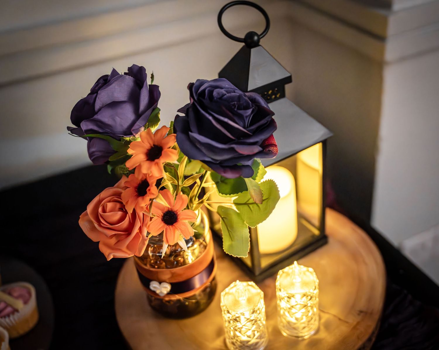 Glowing candle holders and vases with purple and orange flowers create a warm, romantic ambiance on a dark surface.