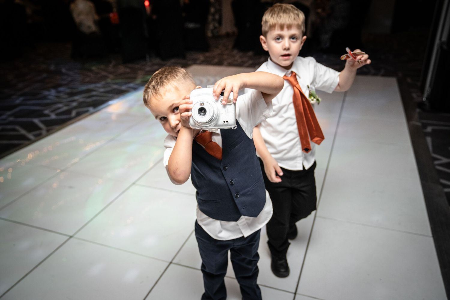 People dancing energetically on a white dance floor at what appears to be a wedding reception.