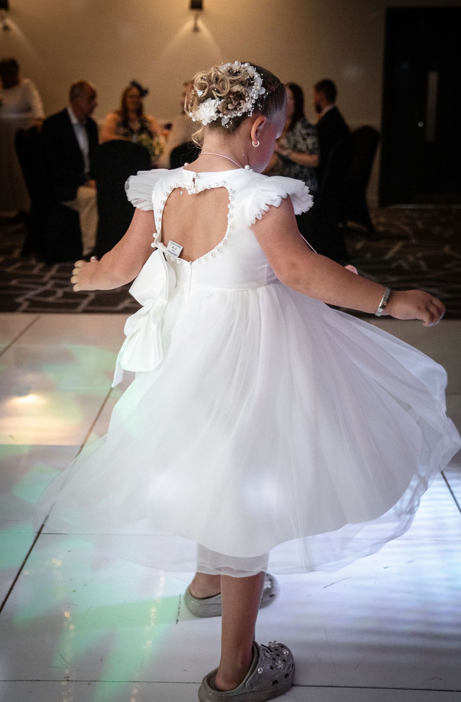 White wedding dress twirling on a dance floor with green lighting effects beneath.