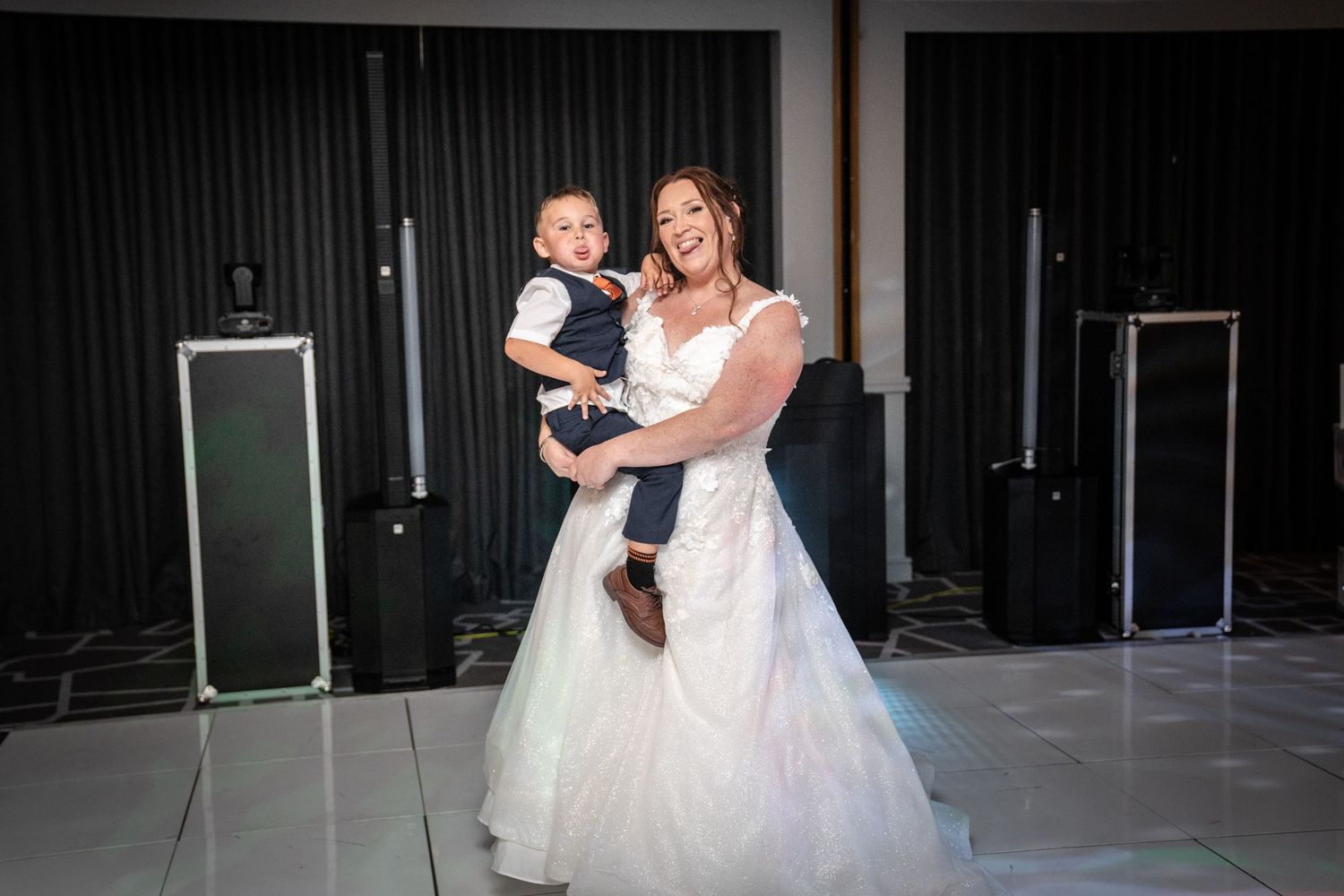 Formal wedding dance shown from behind on an illuminated white dance floor.