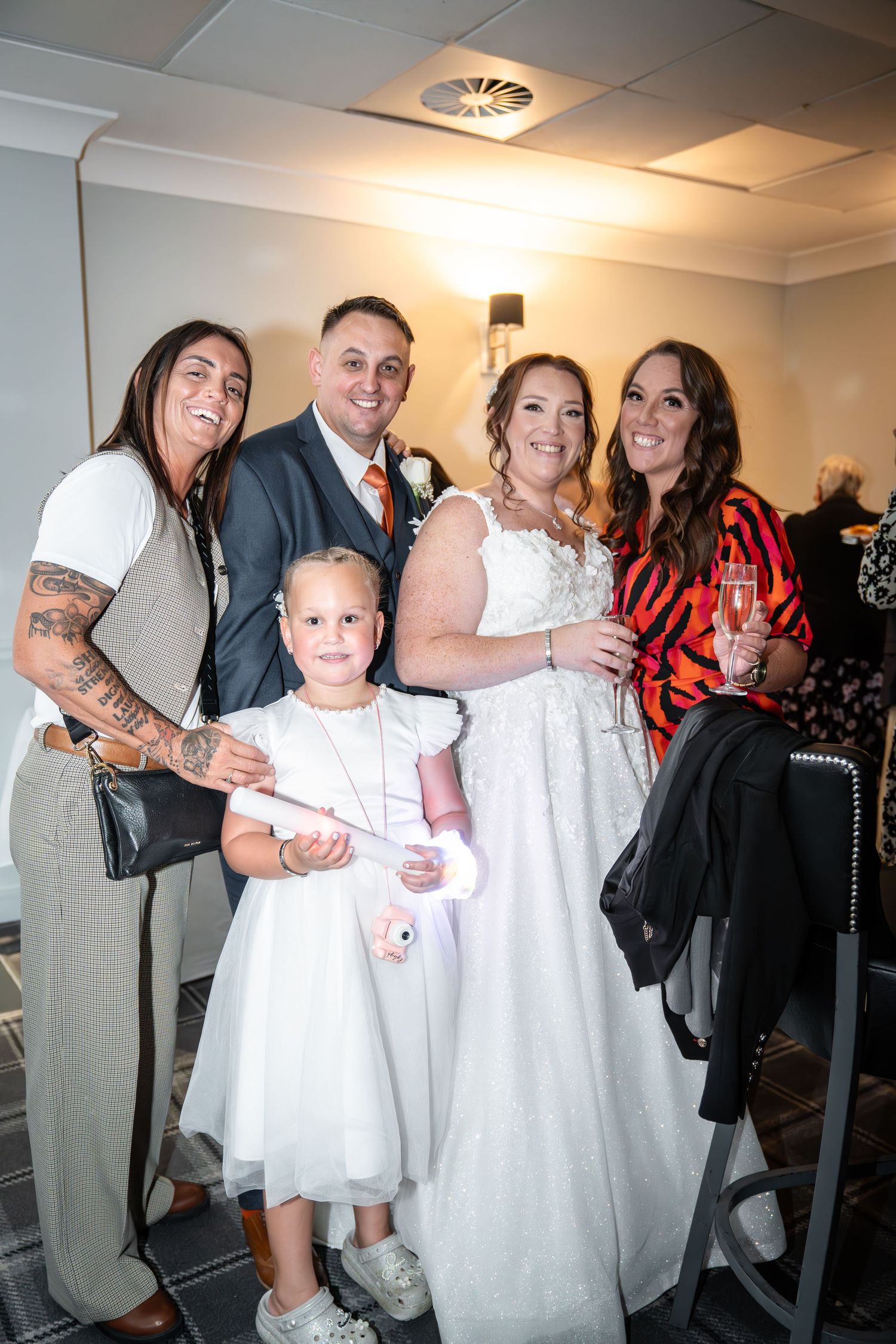 A wedding party poses together indoors in formal attire with a young child in white.