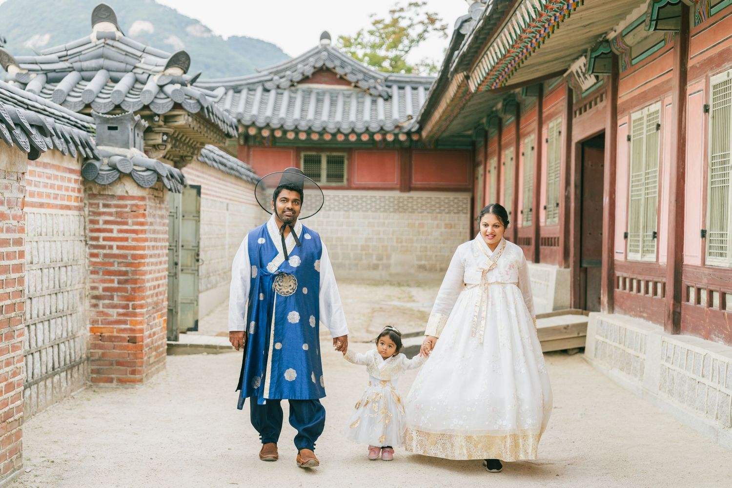 Couple in traditional Korean dress walking through historic palace courtyard.