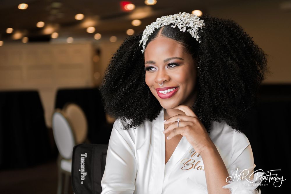 Radiant Black bride in white robe with floral headpiece smiling at wedding reception.