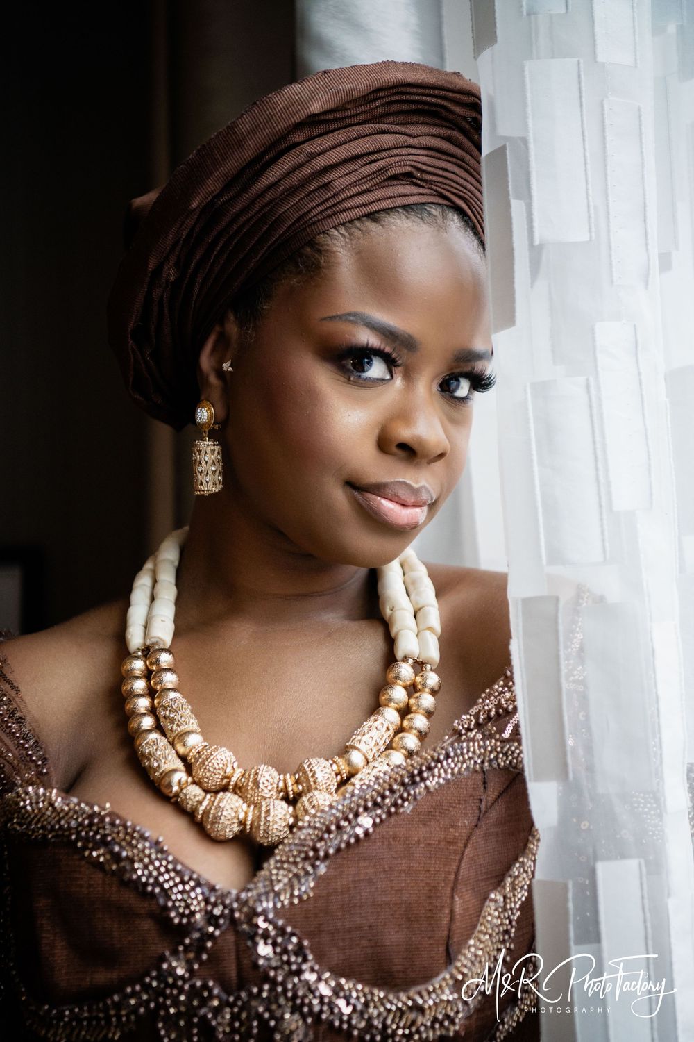 Elegant Black bride in brown traditional attire with gold beaded necklace and head wrap.