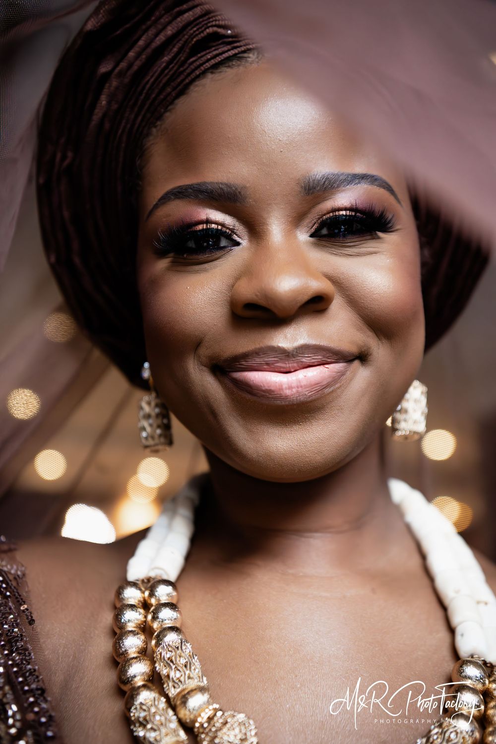 Beautiful Black bride smiling in traditional brown African attire with gold beaded necklace.