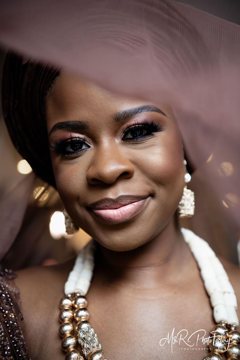 Radiant Black bride in traditional African brown wedding attire with layered gold bead necklace.