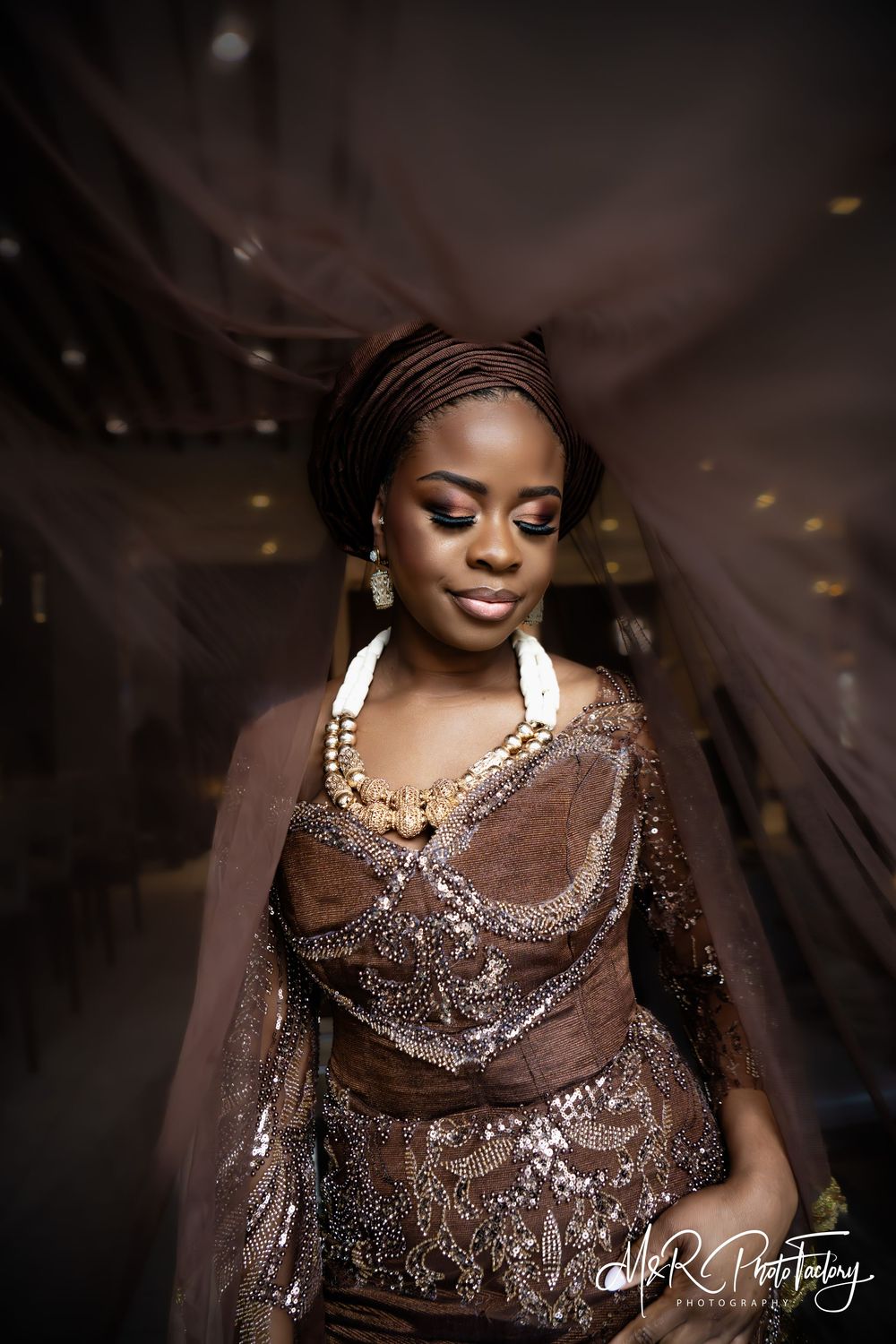 Elegant African bride in brown sequined dress and gele headwrap with gold beaded necklace.