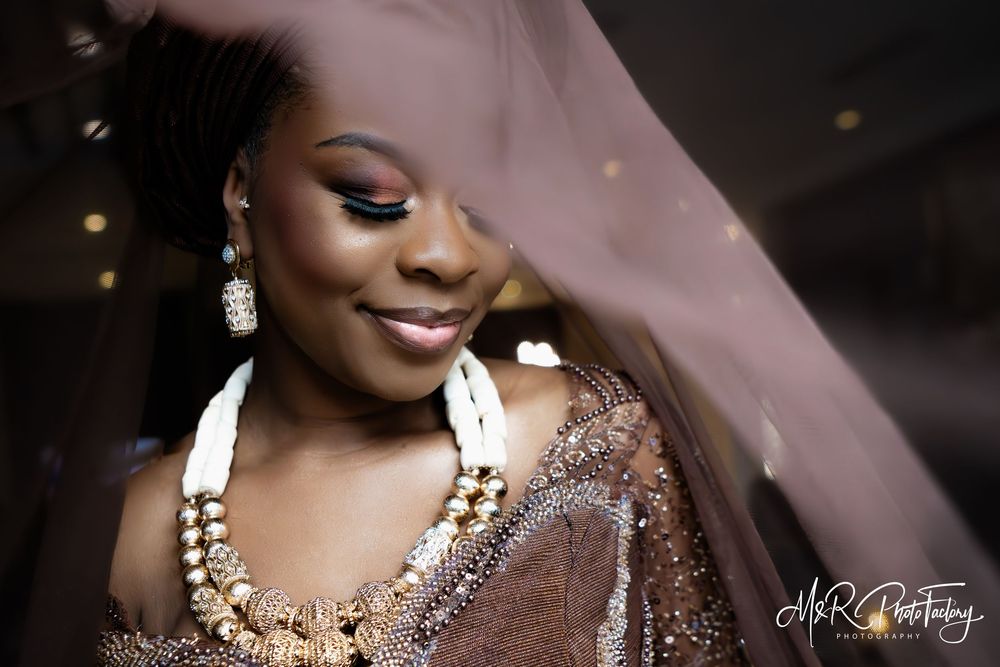 Stunning African bride in sequined brown outfit with white and gold beaded necklace and earrings.