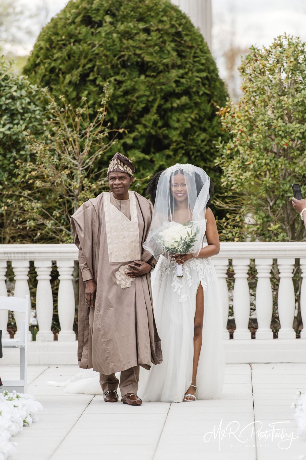 Nigerian father in traditional beige agbada proudly walking daughter in white wedding gown.