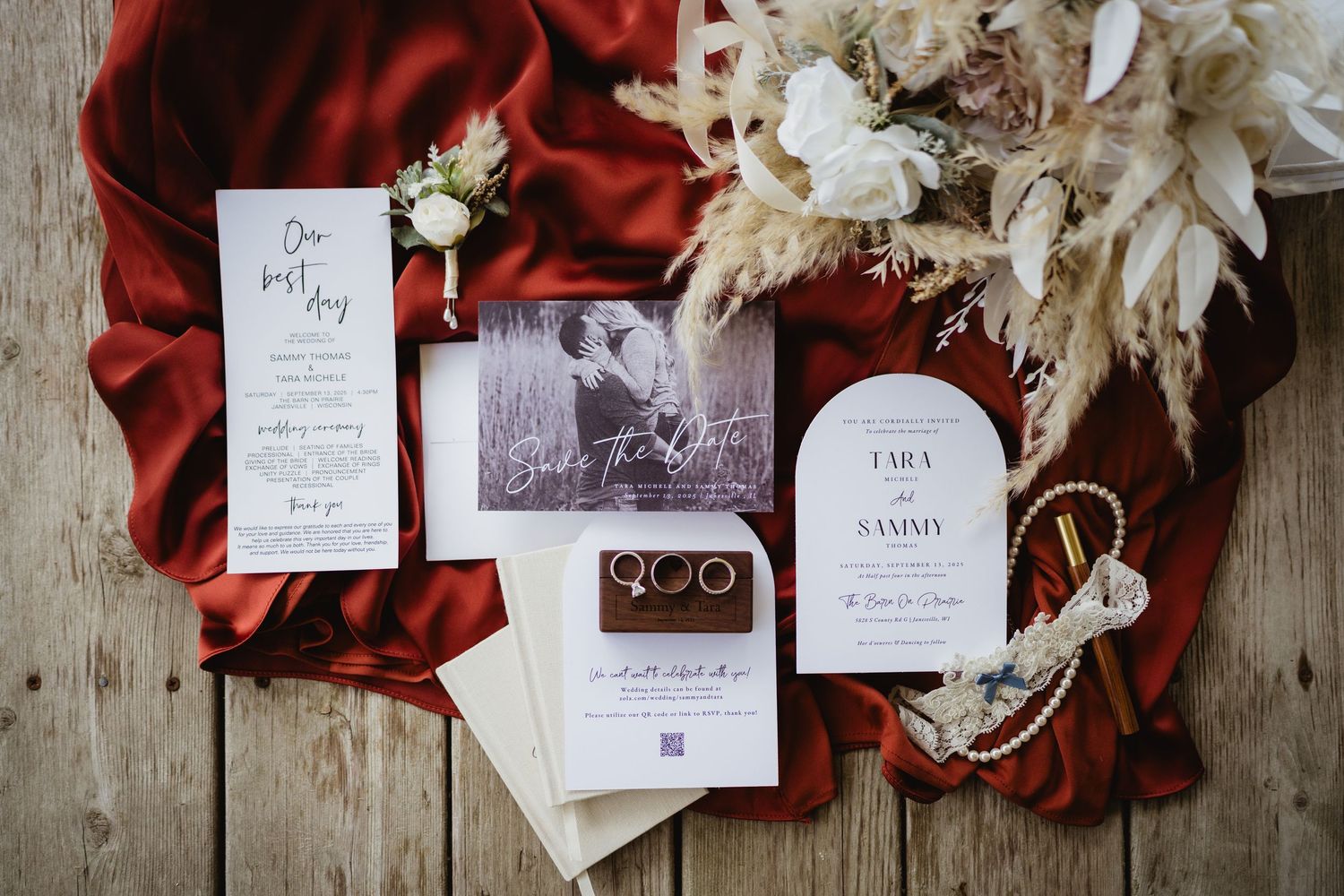 Wedding stationery and dried floral arrangements displayed on rustic wooden surface with rich burgundy accents.