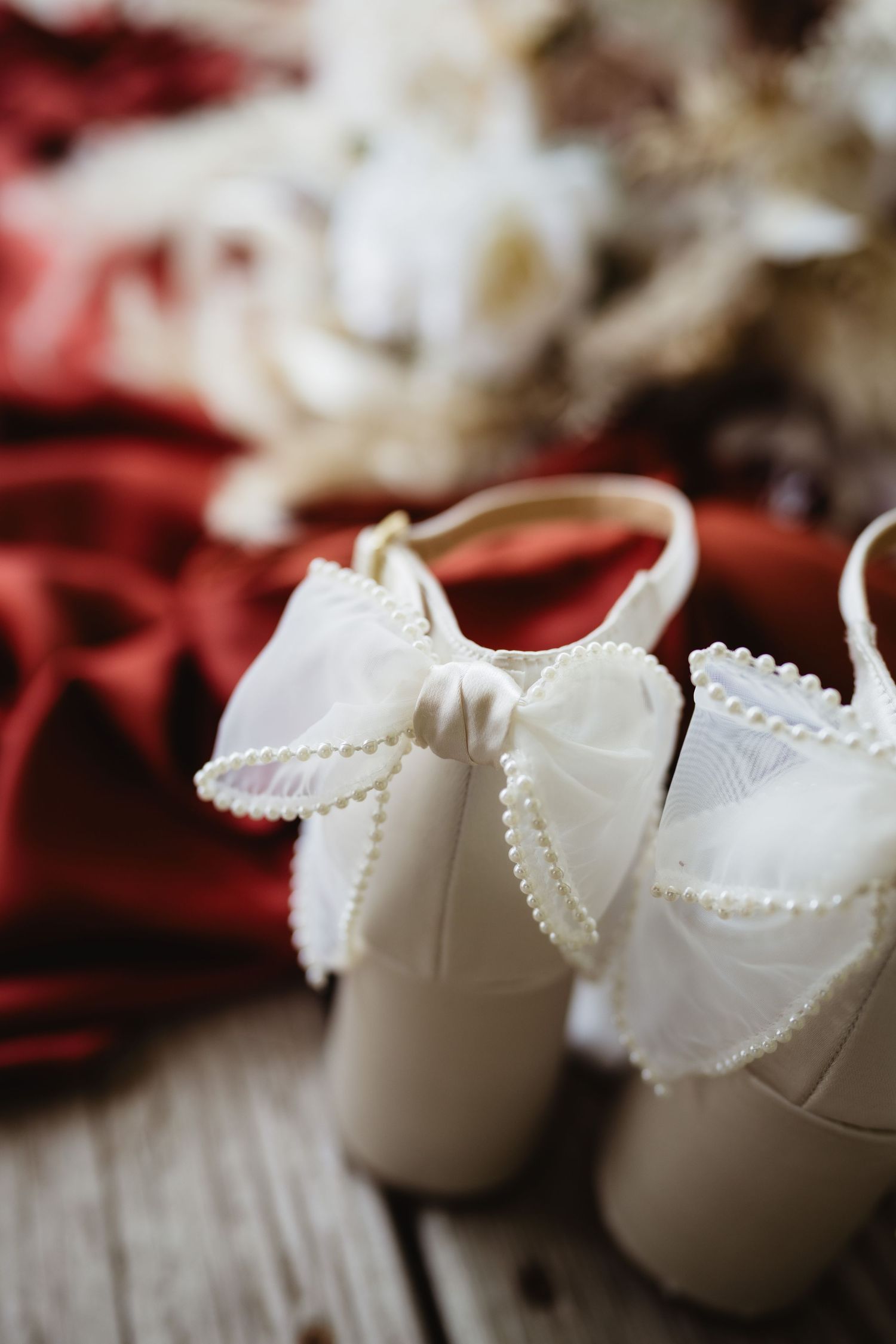 White bridal shoes with delicate pearl details arranged in a repeated pattern detail shot on red background.