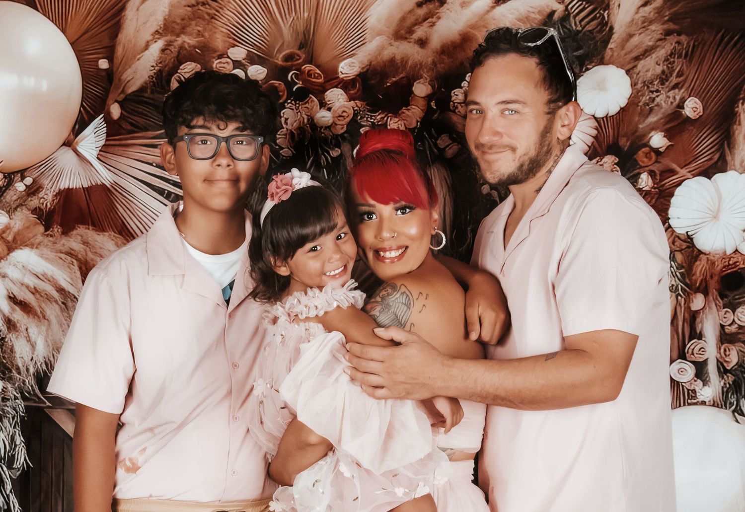 A family poses together under an elegant balloon arch and floral decorations at a special celebration event.